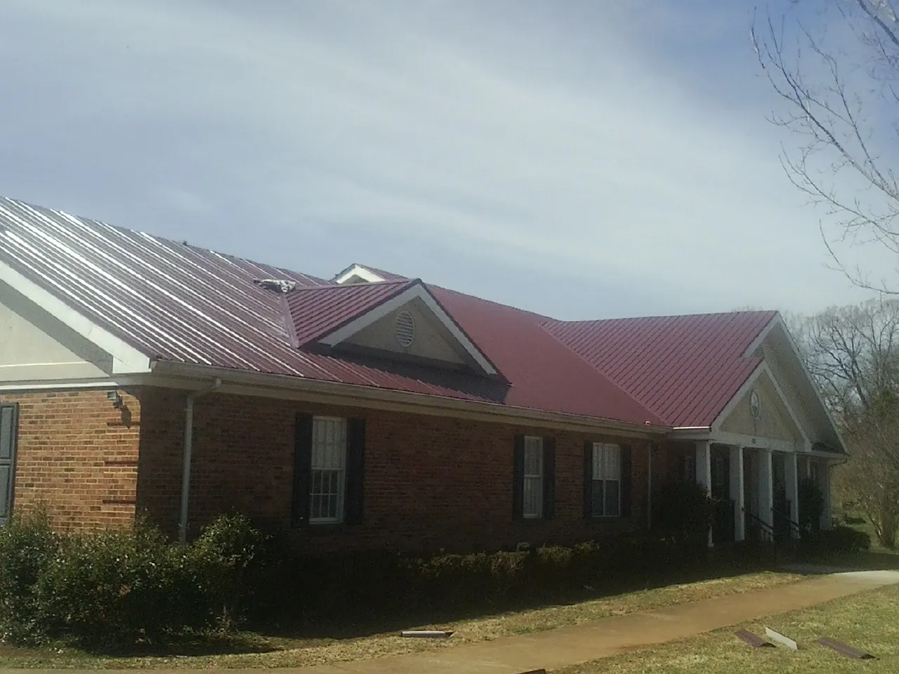 Red metal roof with gabled entries on a long brick building, from a Hail Damage Roof Repair job in Haswell
