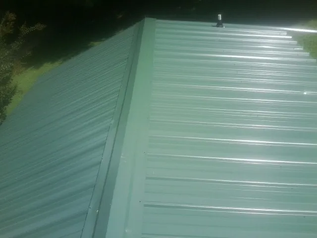 New green metal panels meeting at the ridge of a roof — Flat Roof Repair work by our crew in Haswell