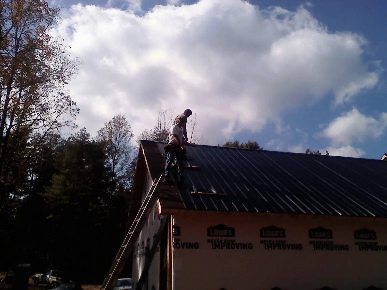 Roofer fastening dark metal panels high against a cloudy sky, from a Roof Inspection job in Haswell