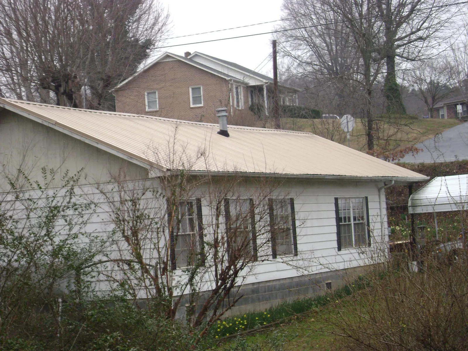 Tan metal roof on a white sided house set into a hillside — Commercial Roofing by Roofing Brothers in Haswell